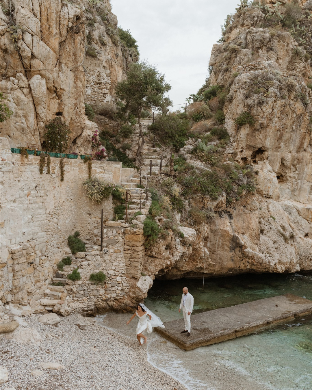 A bride runs along a beach as her groom watches from a stone pier—capturing the elegance, emotion, and premium storytelling that a Showit template for wedding photographers should visually reflect.