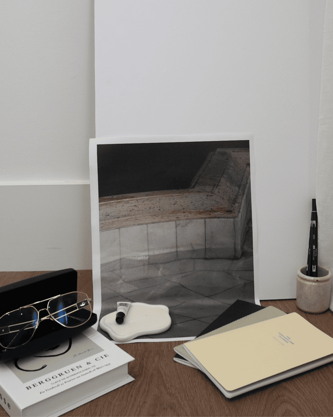 Flat lay of creative desk scene with sunglasses, design books, neutral-toned notebooks, and a modern architectural print—capturing elevated, intentional branding for service-based entrepreneurs.