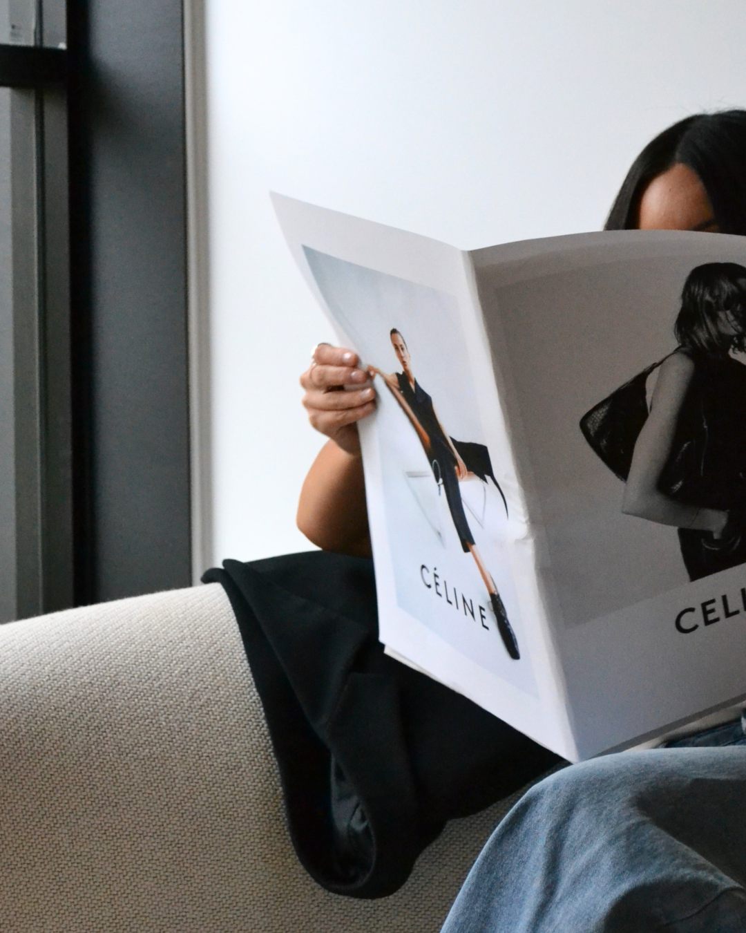 Woman reading a Céline fashion magazine on a modern neutral couch, evoking minimal luxury and strategic brand styling for creative entrepreneurs.